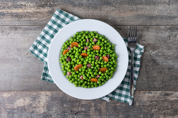 Green peas with serrano ham and carrot on wooden table. Top view