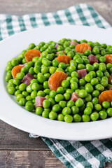 Green peas with serrano ham and carrot on wooden table
