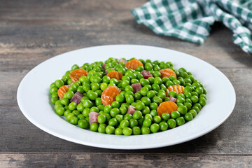 Green peas with serrano ham and carrot on wooden table