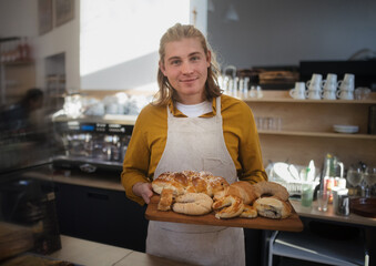 Young man working in cafe, carring fresh pastries.