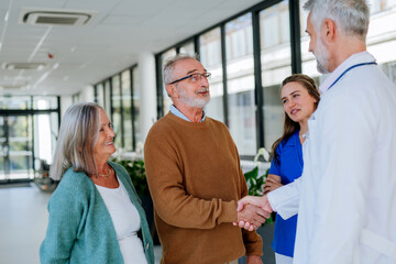 Obraz premium Mature doctor and his young colleague talking with his senior patients at hospital corridor.