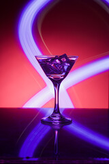Martini glass with ice. On the bar. Against the background of neon light.