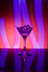 Martini glass with ice. On the bar. Against the background of neon light.