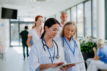 Older doctor giving advise to her younger colleague, discussing at hospital corridor. Health care...