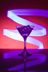 Martini glass with ice. On the bar. Against the background of neon light.