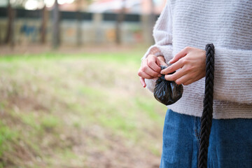 Cropped shot of young woman tying a knot in the dog trash bag after pet in park.