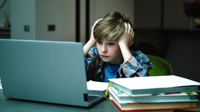 Man Teenager boy Student Being Tired While Using Computer To Study Online Home, teenager boy having headacke or stress while doing homework assignment, sitting with books and looking at laptop screen
