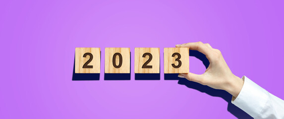 Hand holds a cube with 2022 numbers on wooden blocks. Bright pink background. Hard shadow. New Year's banner. Festive