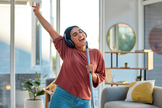 Cleaning, singing and woman dance to music for fun, energy and happiness while doing housekeeping, mop and broom in living room. Spring cleaning, headphones and happy dancing at home with freedom