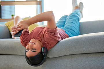 Headphones, phone and woman upside down on sofa in home streaming music, radio or podcast. Relax,...