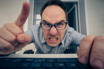 angry hayter writes negative comments on the social network. Negative emotions of businessman employee in front of a computer. malice and hatred concept. offended nerd reads the message on website. - obrazy, fototapety, plakaty