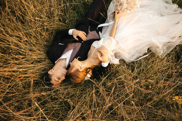 Beautiful young couple bride and groom lie in the grass and hug