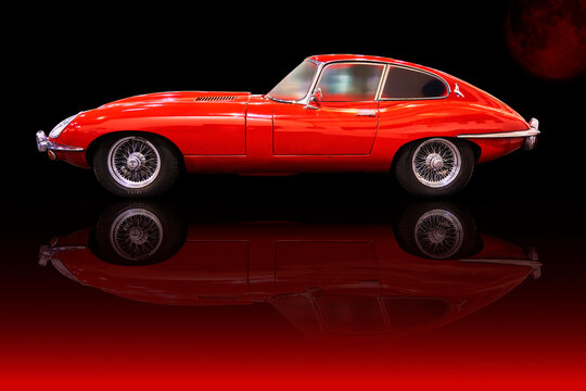 Jaguar E Type in side view, red painted classic sports car from England reflected on the ground, Essen, Germany, December 5, 2022