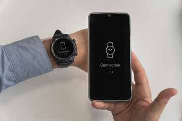 a man is holding a smartphone and a smartwatch in his hand. wireless connection of the watch and...