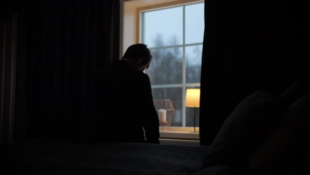 Silhouette of man sitting on bed, window as background. Sadness concept, Shot from behind