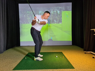 Professional male golfer holding club playing golf indoors on golf simulator