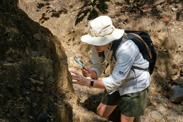 Female geologist using a magnifying glass examines nature, analyzing rocks or pebbles. Researchers...