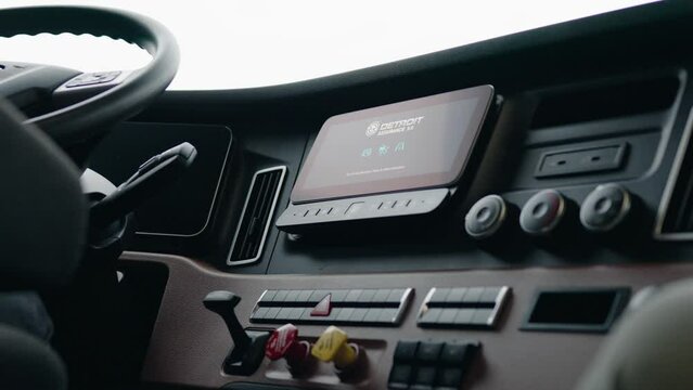 screen turning on of a new freightliner cascadia 2023 Semi Truck. Clean dashboard with modern controls. Driver on the seat. Visible: Parking brakes, screen, temperature controlls, usb chargher, 12 v