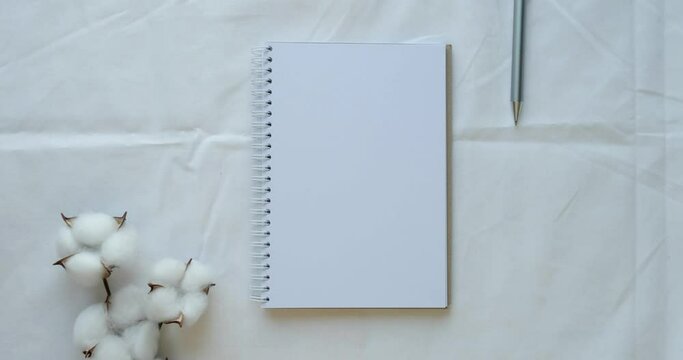 Cozy composition with a clean opened note, pen and cotton branch on a white sheet. Looped 4K stop motion animation
