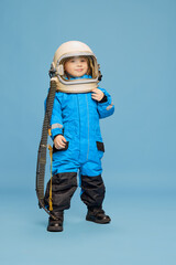 Portrait of little boy, child posing in astronaut costume over blue studio background. Space...