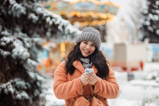 Pretty Long-haired Girl With Smartphone At Winter Snow Park In Cold Weather Scrolling Texting Chatting Using Mobile Phone