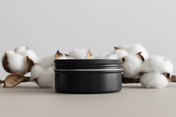 Black cosmetic cream jar mockup with a cotton branch on the beige table.