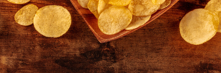 Potato chips or crisps, a salty snack on a wooden background, a panorama with a place for text