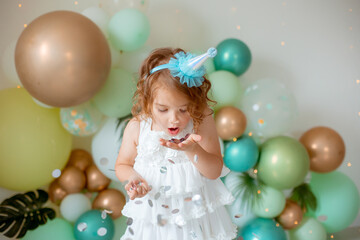 Fototapeta na wymiar A happy little girl in a festive hat blows confetti from her palms
