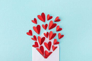 Valentine day greeting card with love message. Envelope and paper red hearts on blue background top view. Flat lay. © juliasudnitskaya