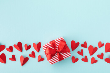 Gift or present box with red ribbon and paper red hearts on table top view. Valentine day background. Flat lay style.