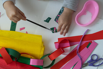 little child makes decorations from colored paper with glue and scissors and paint brush top view...