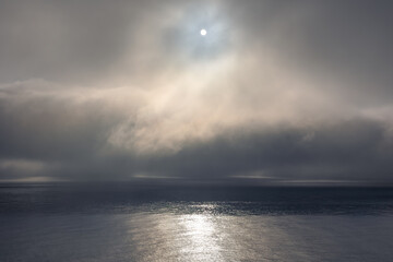 Fog clouds low above the calm water of the Irish Sea and the sun peaking through the clouds. 