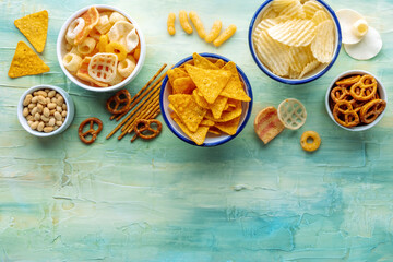 Potato and tortilla chips and other salty snacks, shot from above with copy space. Party food on a purple background. A mix of appetizers in bowls