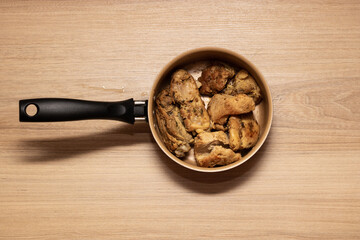 Aluminum pan with chicken meat and plastic handle. Brazilian food on wooden table