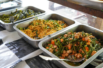Food stalls share a variety of buffet menus with vegetables, chicken curry sauce, beef, eggs, tofu, tempeh. the waiter prepares the food. Menu in glass display case. Asia and asian food. Pile.