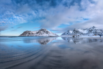 Sandy arctic beach with blue sea reflected in water and rocks in snow in winter at sunset in...
