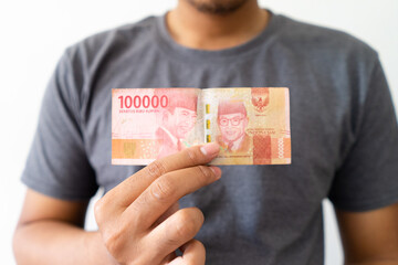 A hand holds a 100,000 Rupiah money with people chest body background