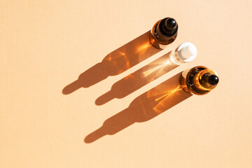 Glass bottles of cosmetic liquids, arranged in a row on the pastel beige surface, cast shadows....