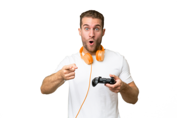 Young handsome man playing with a video game controller isolated on green chroma background surprised and pointing front