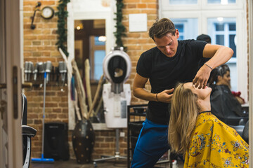 Hairstylist during work. Expert hairdresser cutting his client's blond hair in an unconventional way. Interior of beauty salon. High quality photo