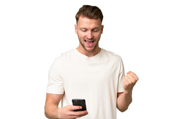 Young blonde caucasian man over isolated background with phone in victory position