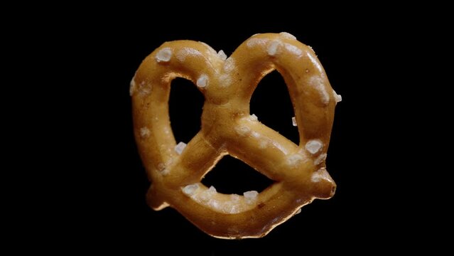 mini pretzel rotates on a black background, super close-up, you can see all the grains of salt.