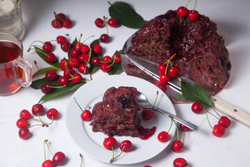 Chocolate cake with sweet cherry, cup of tea and bouquet of blue flowers on white background..