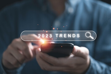 Businessman holding smartphone with searching bar with 2023 trends year for marketing monitor and...