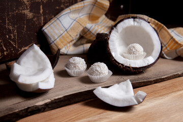 Coconut with white pulp and white candies on wooden background..