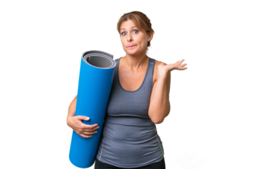 Middle-aged sport woman going to yoga classes while holding a mat over isolated background having doubts while raising hands