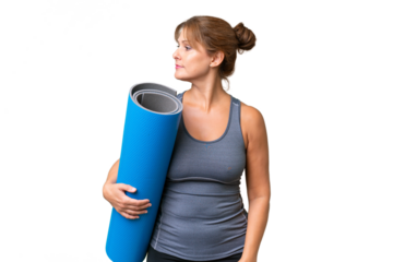 Middle-aged sport woman going to yoga classes while holding a mat over isolated background looking to the side