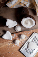 Close up of coconut with white pulp, grater with coconut chip and white candies on wooden background..