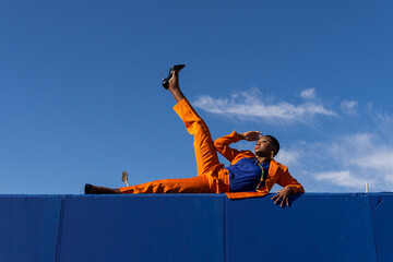 Stylish ethnic woman lying on blue fence