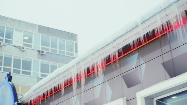 Large icicles hang from the overhang of the roof of the building. Falling ice- winter hazard for passersby